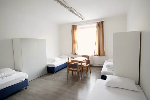 Világos szoba ágyakkal, szekrényekkel és étkezőasztallal